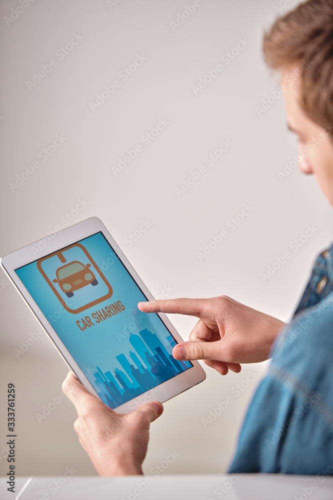 Poster Over shoulder view of guy using car sharing app on tablet while finding suitable car for trip