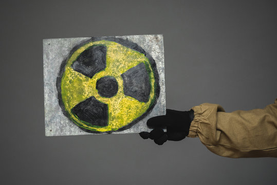 Radiation symbol on the rusty plate in the hand on gray background.