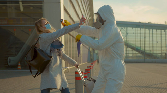 Medical worker in a protective suit try screening passenger to check woman sprinkles an antiseptic on it Covid-19 symptoms coronavirus checkpoints airports mask infection epidemic corona slow motion