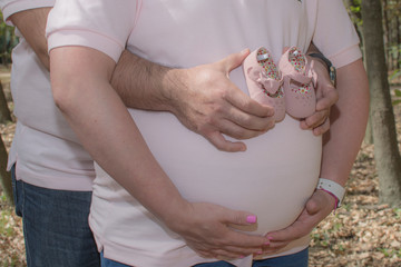 Mujer embarazada con las manos de ella sosteniendo su barriga y las manos del papá sosteniendo unos zapatos del bebé a nacer: es niña