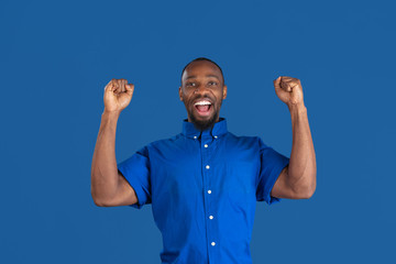 Crazy happy winner. Monochrome portrait of young african-american man isolated on blue studio...