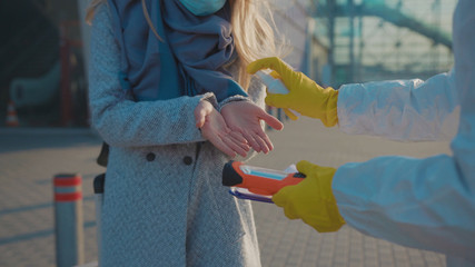 Close up hands medical worker in a protective suit sprinkles antiseptic woman on hands Covid-19...