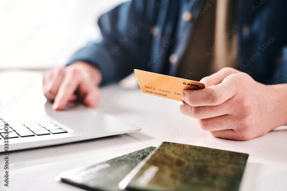 Aufkleber Close-up of unrecognizable man sitting at table and using laptop while paying online with bank card