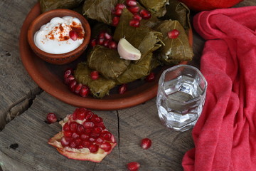 Dolma in a clay plate with pomegranate, sour cream and chacha on a wooden background