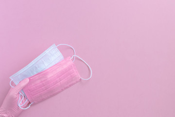 Pink protective surgical face mask and woman hands in gloves background, selective focus