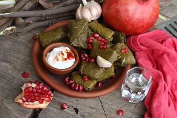 Dolma in a clay plate with pomegranate, sour cream and chacha on a wooden background