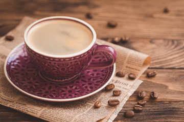 Cup of coffee with beans on newspaper background, business breakfast concept, selective focus, toned vintage