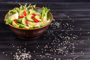 Salad of fresh cucumbers, spinach leaves, arugula, avocado. Served with slices of eggs and red pepper. Dietary nutrition. Breakfast for the whole family. Vitamin plate. On a dark wooden background.