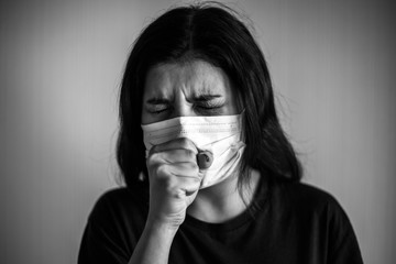 Portrait of a young woman wearing medical sterile mask, coughs and covers with her hands. Dramatic black and white closeup of a girl being protected from coronavirus. Quarantine stay home concept.