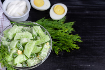 Salad of fresh cucumbers, spinach leaves, arugula, avocado. Served with slices of eggs and red pepper. Dietary nutrition. Breakfast for the whole family. Vitamin plate. On a dark wooden background.