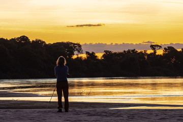 Pessoa observes the exuberant sunset in the autumn afternoon in the Brazilian savannah at Praia do Sol, on the banks of the Rio do Coco, a tributary of the Araguaia River.