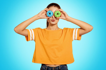 Beauty girl holding blue and green donuts laughing over white background. Beautiful Happy Young woman on party blue doughnuts in a yellow shirt. Joyful model Celebrating. Kiss, lips.