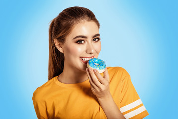 Beauty girl holding blue donuts laughing over white background. There is a dessert, a smile. Beautiful Happy Young woman on party with doughnuts in a yellow shirt. Joyful model Celebrating.