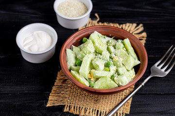 Salad of fresh cucumbers, spinach leaves, arugula, avocado. Served with slices of eggs and red pepper. Dietary nutrition. Breakfast for the whole family. Vitamin plate. On a dark wooden background.