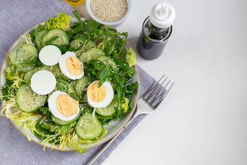 Salad of fresh cucumbers, spinach leaves, arugula, avocado. Served with slices of eggs and red pepper. Dietary nutrition. Breakfast for the whole family. Vitamin plate. On a light background.