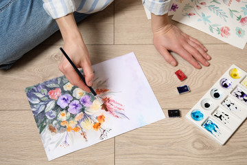 Obraz premium Woman painting flowers with watercolor on floor, closeup