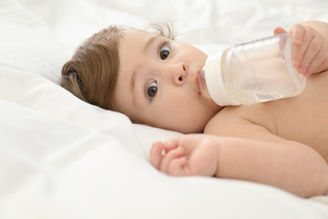 Cute little baby with bottle on bed