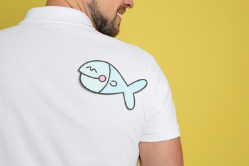 Man with paper fish on back against yellow background, closeup. April fool's day