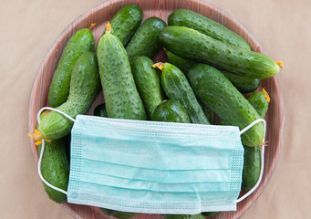 Fresh green vegetables cucumbers under a medical mask. Harvest 2020. Damage to agriculture from coronavirus.