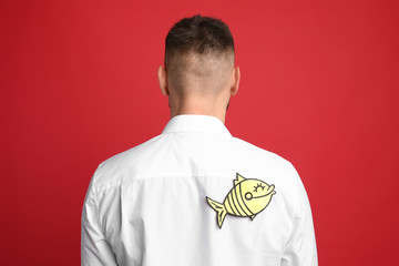 Man with paper fish on back against red background. April fool's day