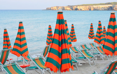 Abandoned parasols and beachchairs in bright orange and green on a small sandy beach in puglia, the...