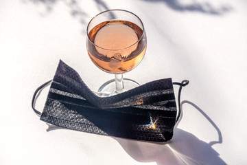 Medical face mask black next to a glass of rose wine on a white background copy-space. Concept of...