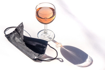 Medical face mask black next to a glass of rose wine on a white background copy-space. Concept of social activities during pandemic and crown virus quarantine.
