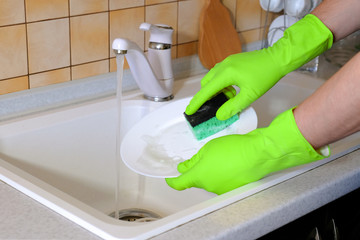 A man washes dirty dishes with a sponge and rubber gloves. Washing dishes in the kitchen.