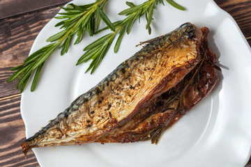 Roasted mackerel with rosemary. in a white plate on a wooden countertop. close-up