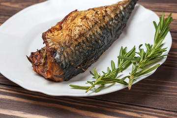 Roasted mackerel with rosemary. in a white plate on a wooden countertop. close-up