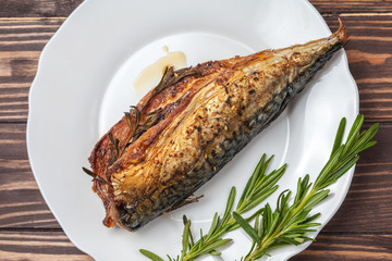 Roasted mackerel with rosemary. in a white plate on a wooden countertop. close-up