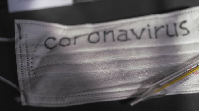 Coronavirus. Medical disposable gauze bandages are on the table. A mercury glass thermometer rests on a protective medical mask.