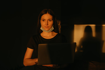 A woman in the removed medical face mask working remotely on her laptop during the quarantine to...