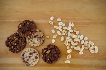 Top view photo of two types of cookies and different nuts on a wooden table top. Chocolate chip cookies and peanut chocolate cookies. 