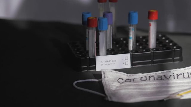 Coronavirus. Medical test tubes are in the organizer. Medical disposable gauze bandages are on the table. A mercury glass thermometer rests on a protective medical mask.