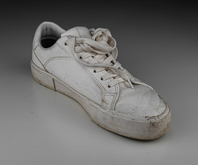 Dirty, used, muddy white left shoes on white dirty floor