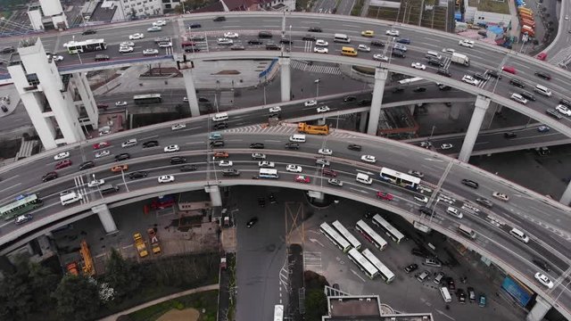 Large road rings of complex stacked interchange at exit from Nanpu bridge, aerial shot. Camera turn right, panning along circular flyover. Busy traffic at evening time in Shanghai city