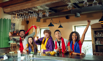 Sport fans cheering at bar, pub and drinking beer while championship, competition is going. Multiethnic group of friends excited watching translation. Human emotions, expression, supporting concept.