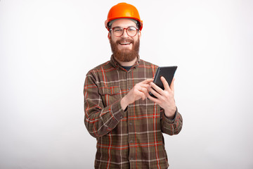 Smiling man wearing hard hat is using a tablet on white background.