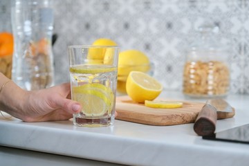 Female hand with slice of lemon in kitchen, with sparkling water with lemon