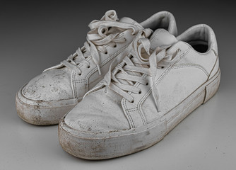 Dirty, used, muddy white dirty pair of shoes on white dirty floor