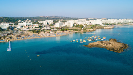 Fototapeta premium Aerial bird's eye view of Fig tree bay in Protaras, Paralimni, Famagusta, Cyprus. Tourist attraction golden sandy beach with boats, sunbeds, sea restaurants, water sports on summer holidays from above