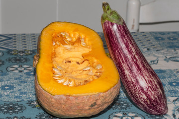 Colorful pumpkin  with aubergine  in the kitchen cut in half accompanied by other food products also suitable and healthy for the food diet 