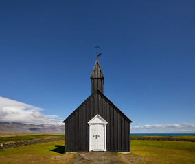 Black wooden church Budakirkja at Snaefellsnes peninsula, Budir village, Western Iceland, Europe. Summer landscape with chapel, mountains and flowers. Famous landmark. Travelling concept background.