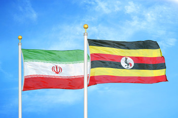 Iran and Uganda two flags on flagpoles and blue cloudy sky