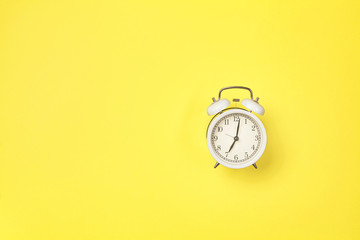 White alarm clock on yellow background with copy space.