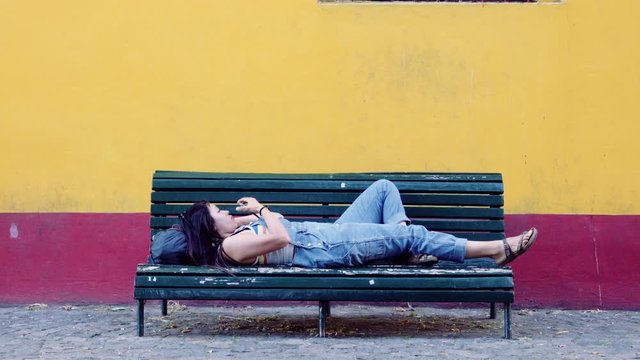 Hispanic woman lay down on the bench texting with a smartphone. 4k