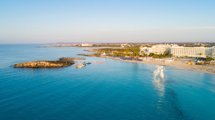 Aerial bird's eye view of famous Nissi beach coastline, Ayia Napa, Famagusta, Cyprus.Landmark tourist attraction islet bay at sunrise with golden sand, sunbeds, sea restaurants in Agia Napa from above