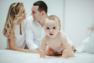 Smiling young couple playing with their beloved newborn baby girl on the bed