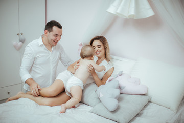Fototapeta premium Smiling young couple playing with their beloved newborn baby girl on the bed